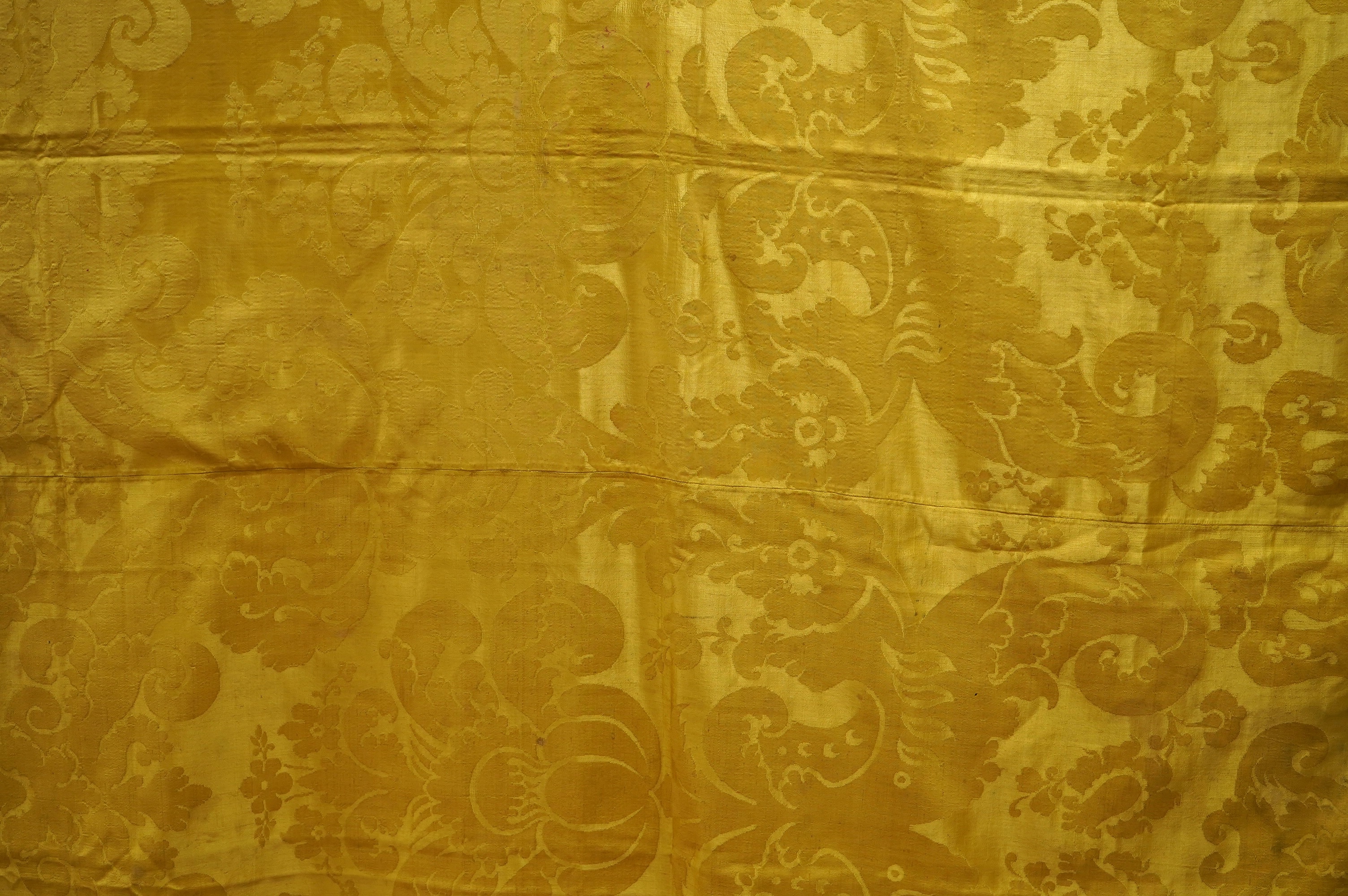 A 19th century gold and crimson silk damask bed cover, the centre being short loom widths of gold damask in a large repeating design, the outer panel a similar crimson damask, both finished with decorative gold braid bor